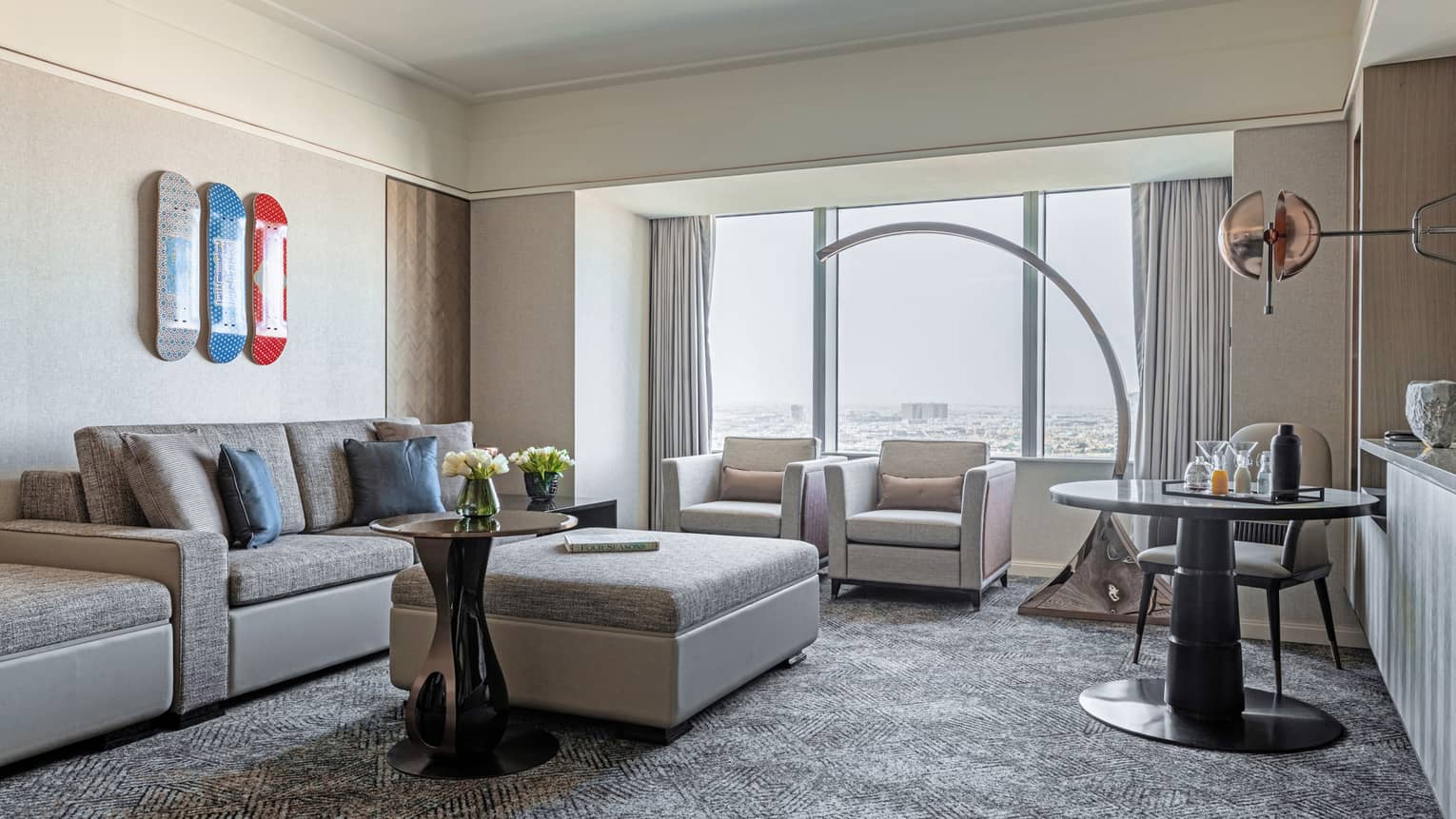 Living room with grey carpet, light grey sofa and ottoman, large curved floor lamp, windows