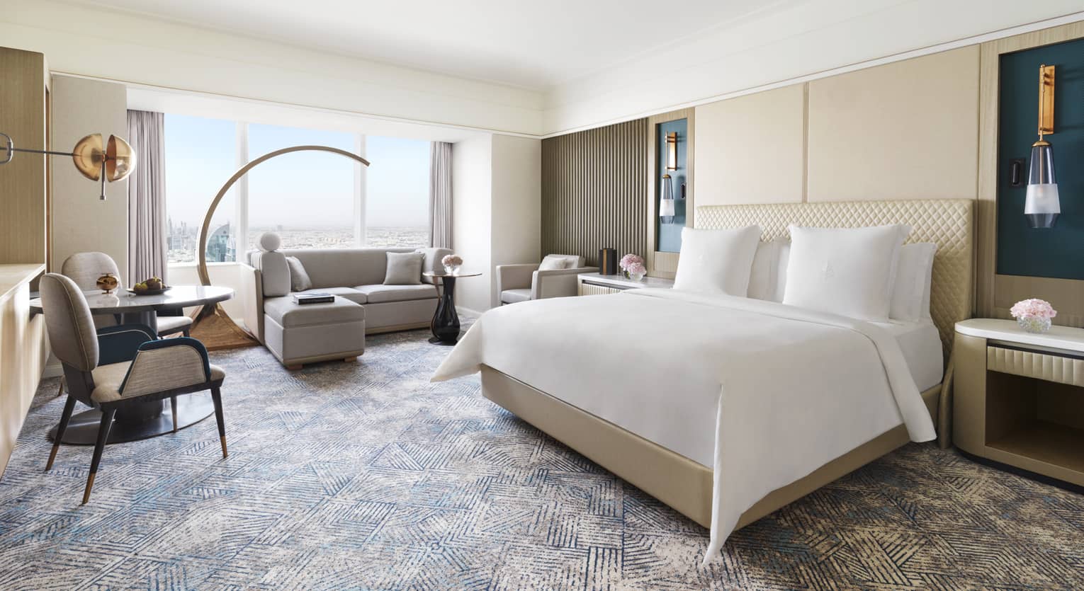 Hotel room with king bed, window-side sofa, and small table with two chairs