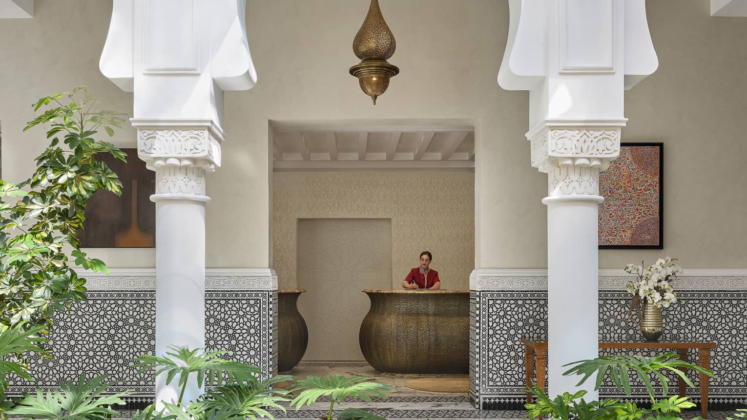 Woman at reception desk at Moroccan hotel with atrium and greenery