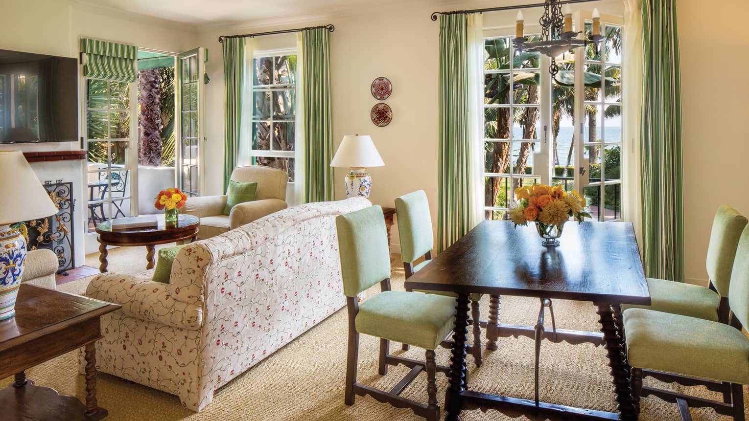 Mariposa Suite dining table behind white floral sofa, armchair, round table, TV