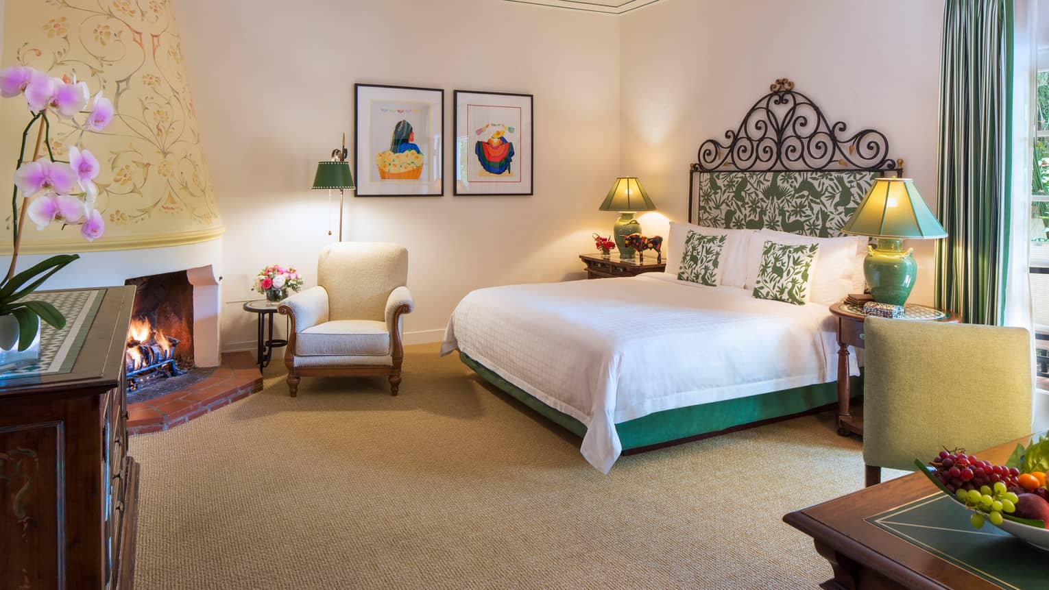 Jungle Room bed with iron and green-padded headboard, white armchair by fireplace, desk, fruit bowl