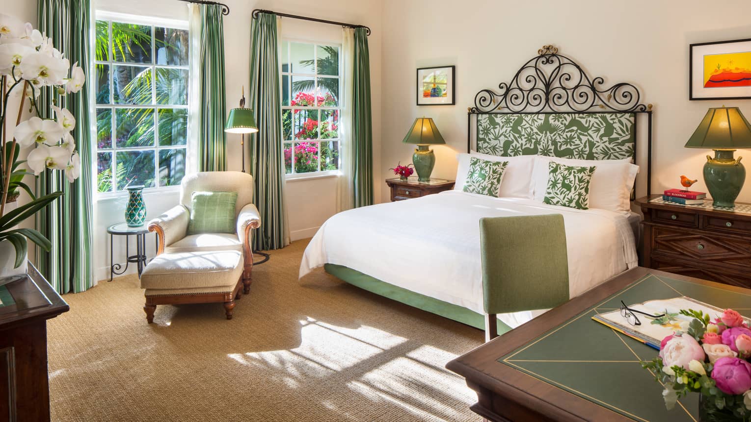 Riviera Room white armchair, ottoman, green pillow under sunny windows by bed, desk