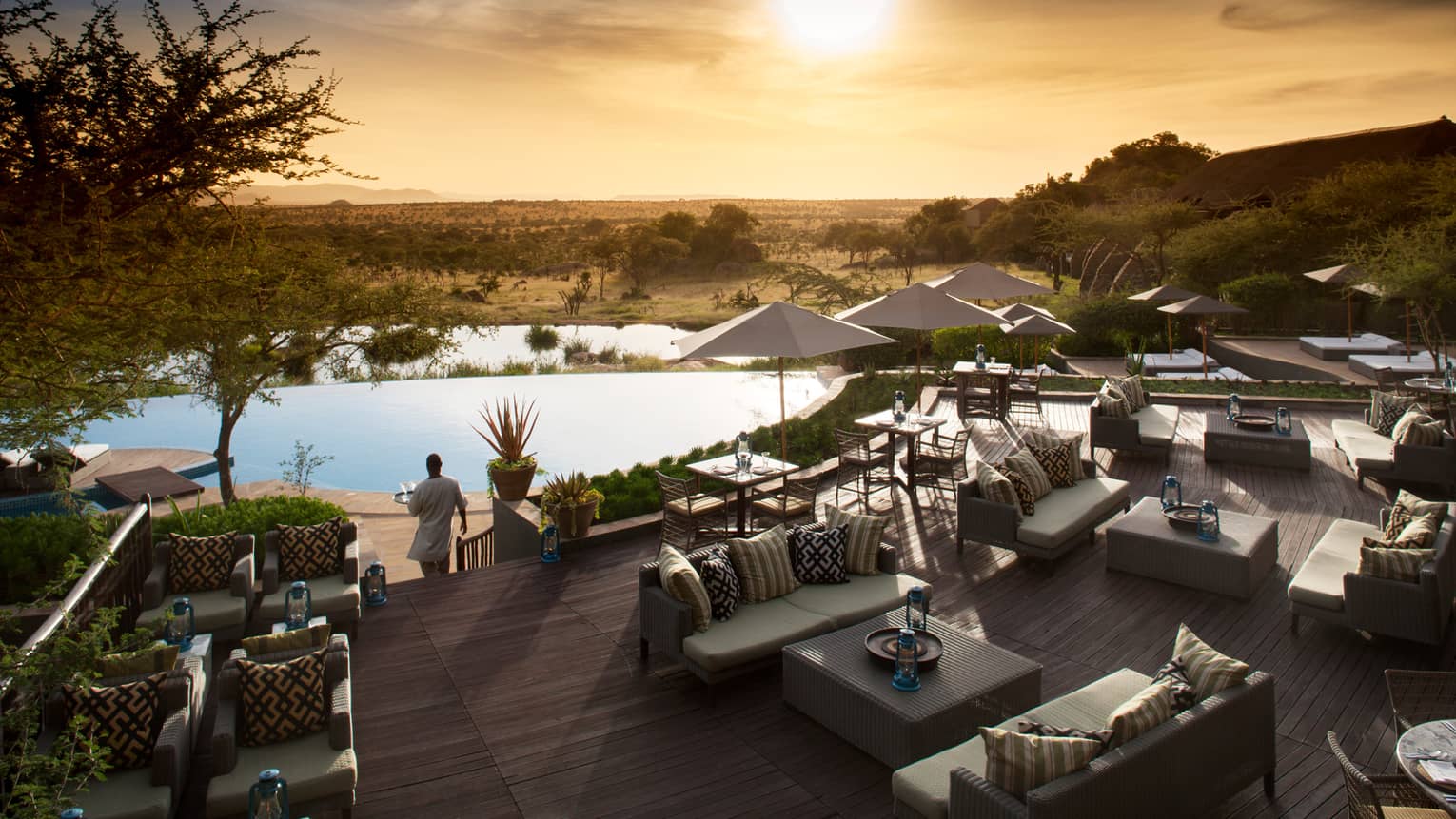 Server carries tray through Terrace Bar outdoor patio by lounge chairs, swimming pool at sunset