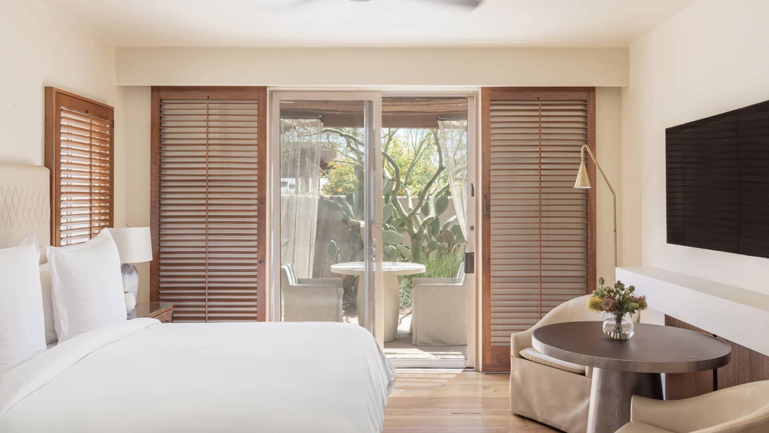 A room with a bed, large glass doors leading outside, two chairs and a small table.