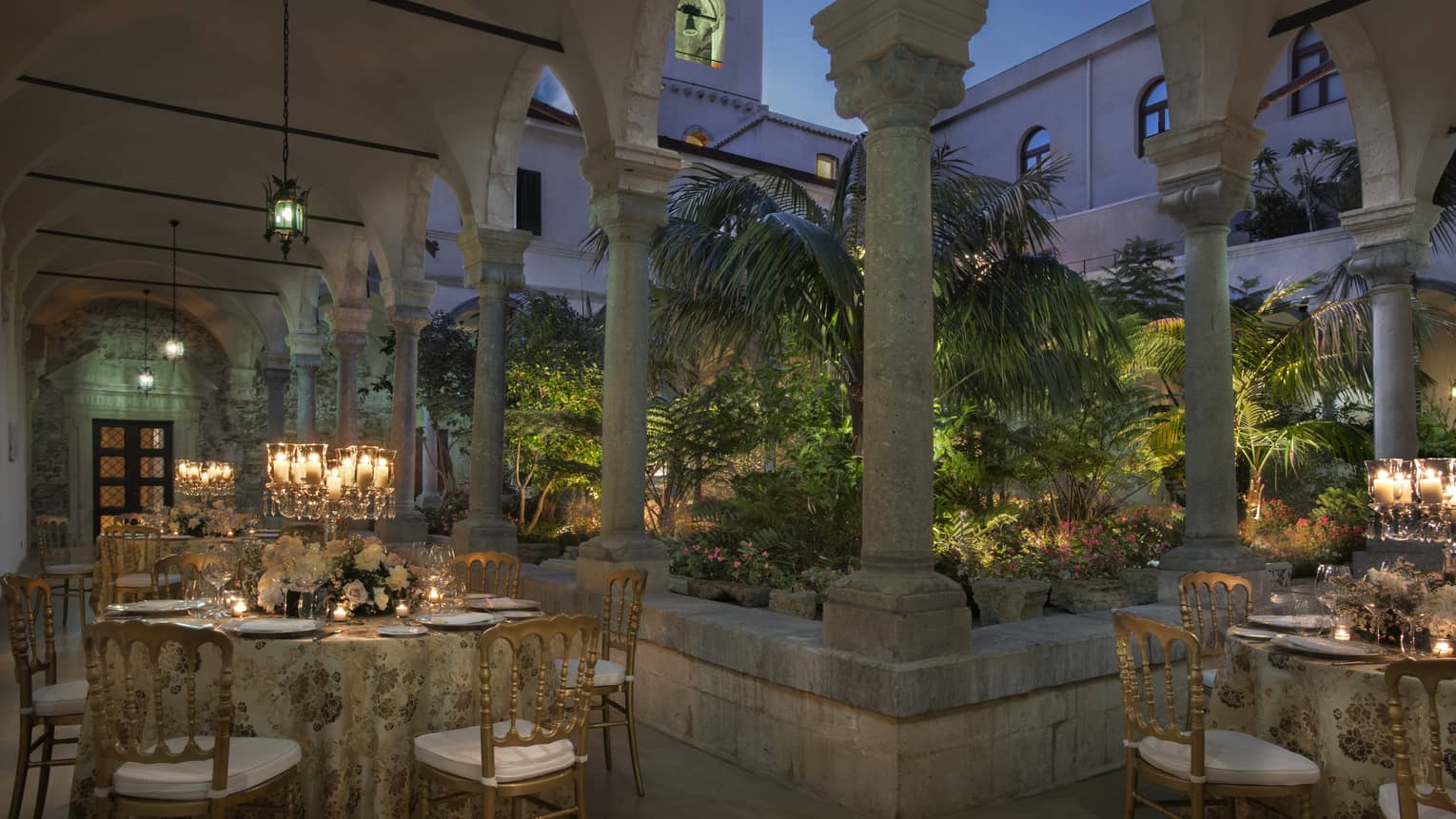 Ancient Cloister outdoor venue with elegant table settings under stone archway at dusk