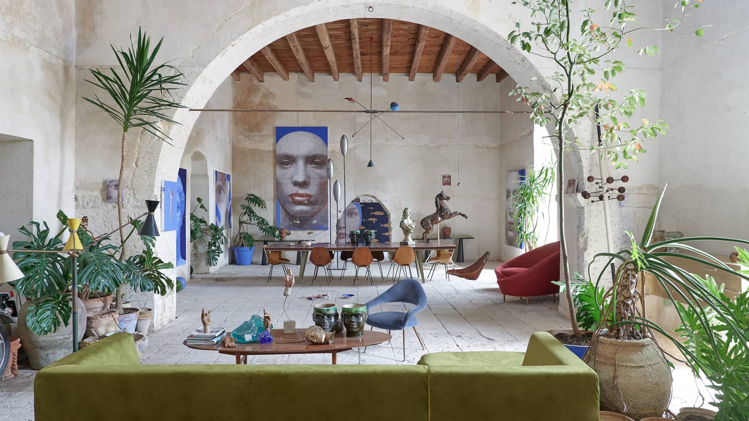 Large room with tropical plants, contemporary furnishings, an arched stone wall and artwork in the distance