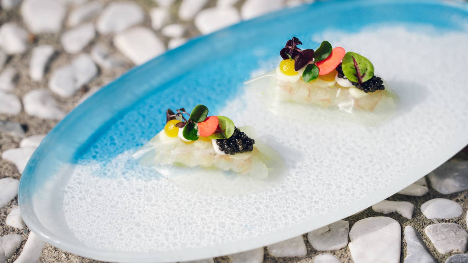 Two langoustine topped with flower garnish on blue-and-white oval-shaped plate