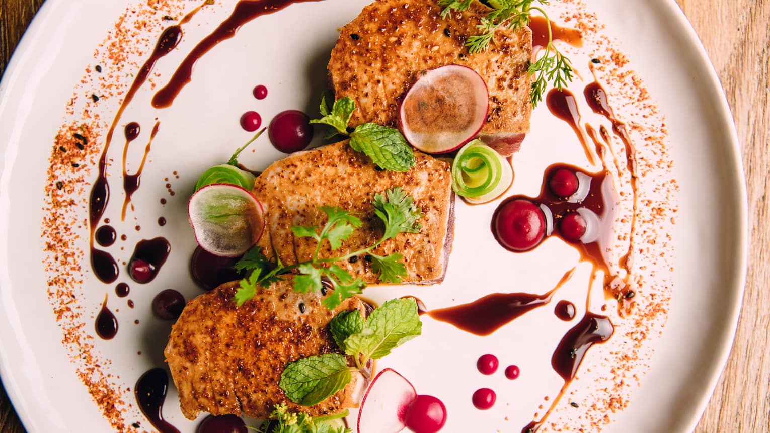 Three seasoned fish fillets with herb garnish, radishes and sauce surround on white plate