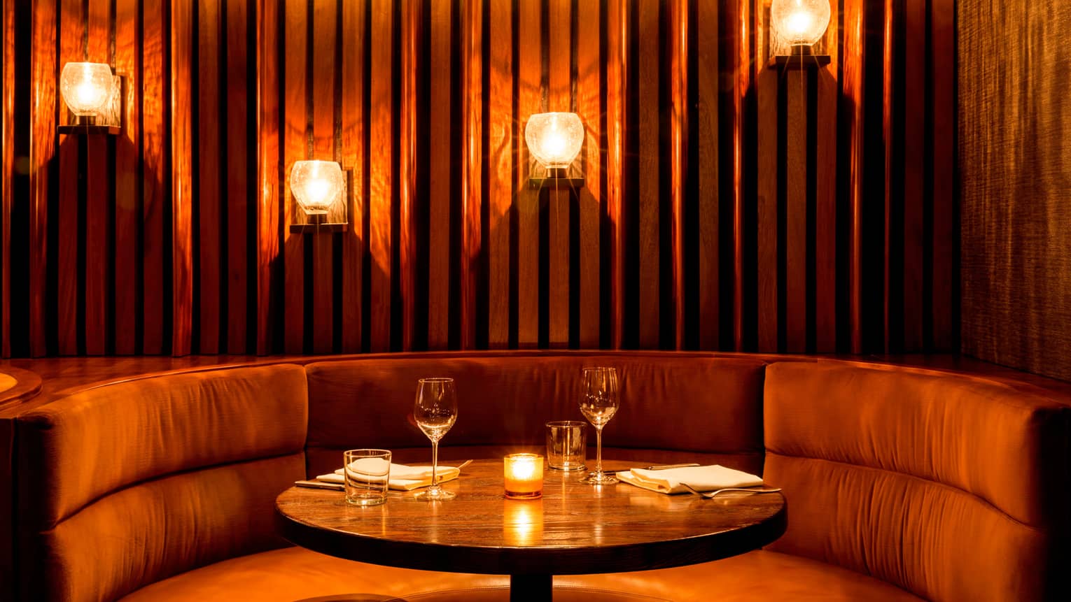 Curved plush banquette with candles, warm lights on panel wall