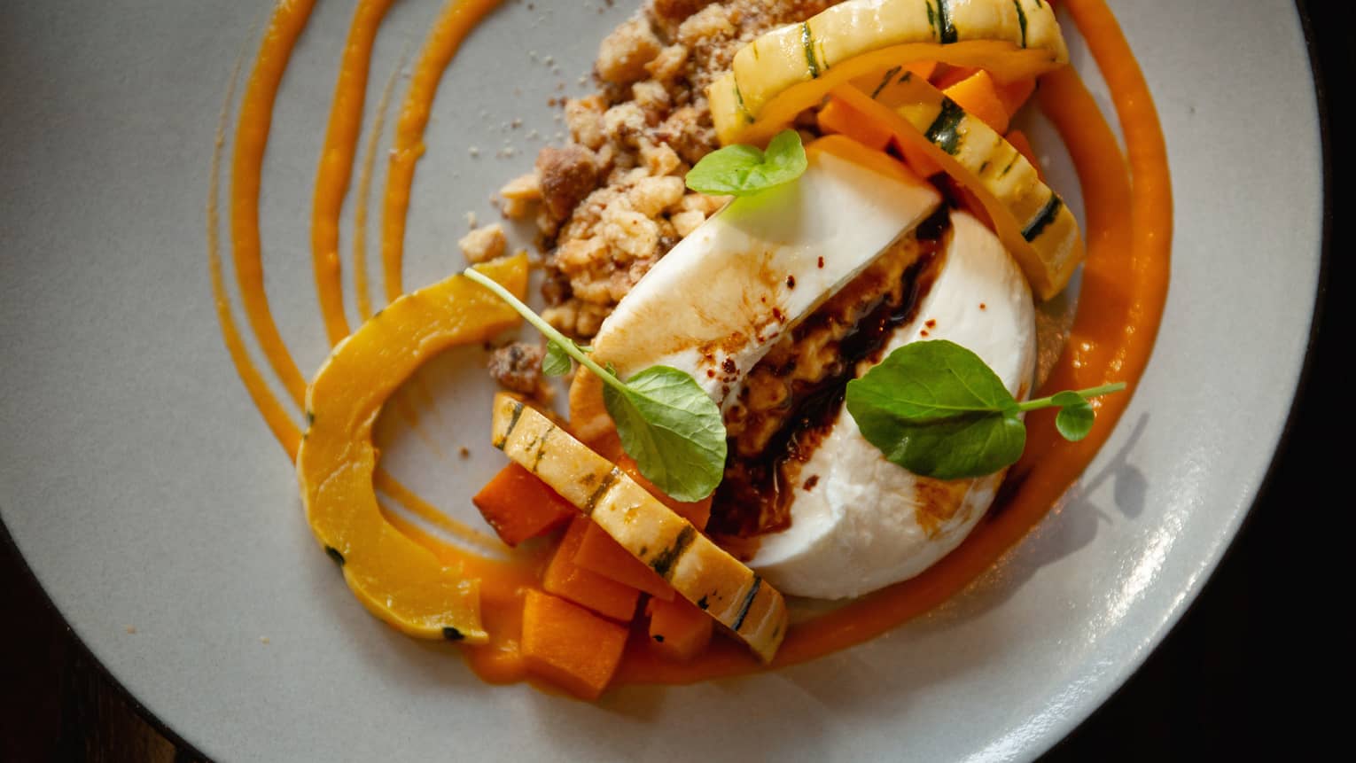 A dish of fermented butternut squash, pomegranate molasses, roasted delicata squash, aleppo spiced walnuts, baguette