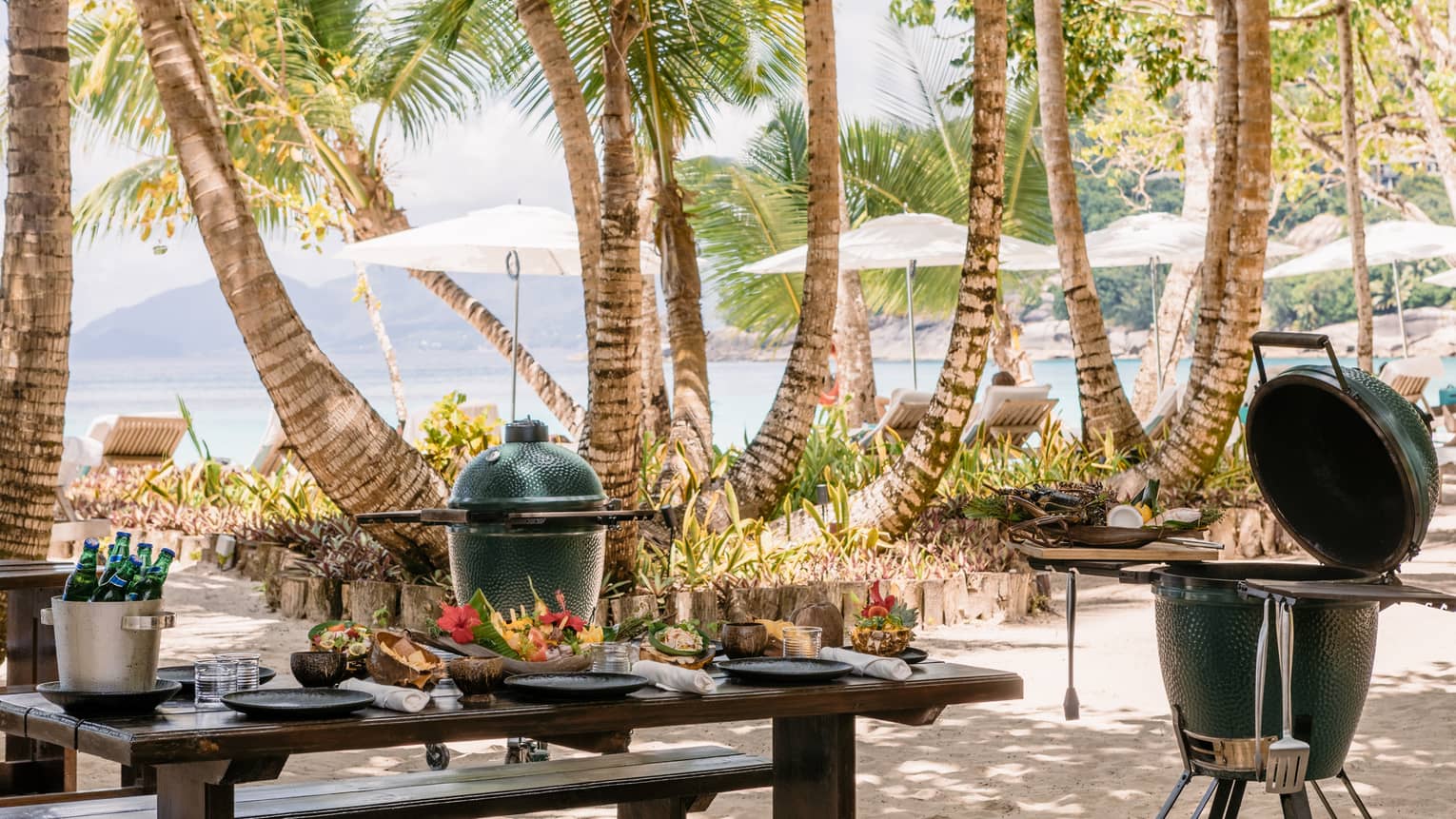 BBQ and grill equipment outside near a table and palm trees.