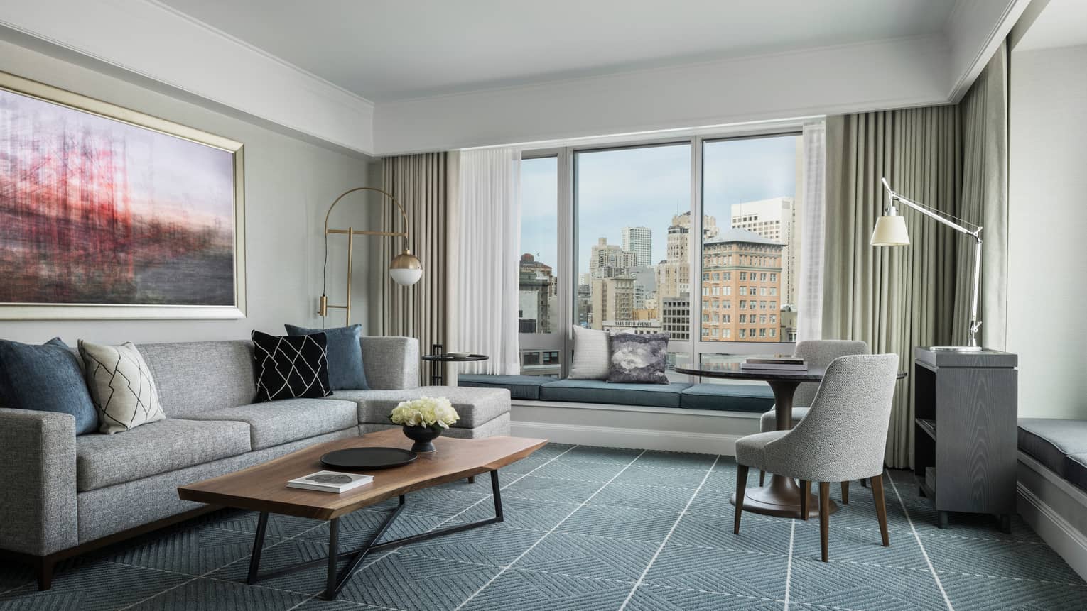 Hotel room with modern seating area, grey sofa by large window with padded bench