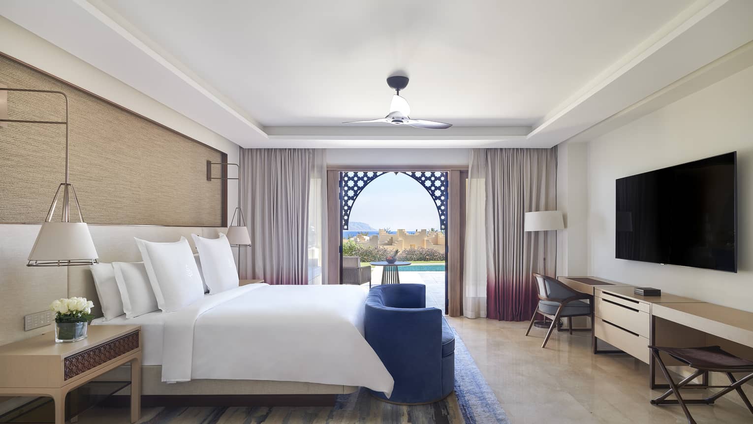 Hotel bedroom with king bed, blue sofa at foot of bed, sea-view terrace