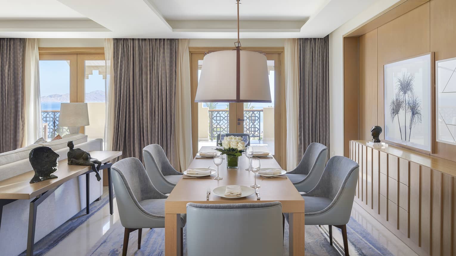 Light wood dining table with six blue chairs, hanging light