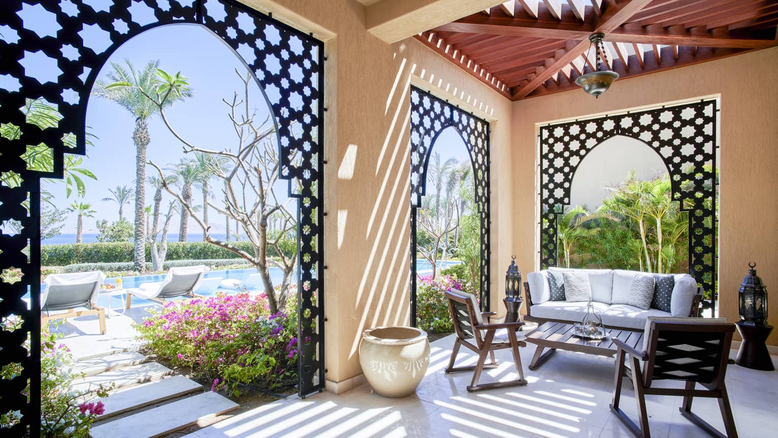 Covered outdoor patio with sofa and two chairs, close to a pool