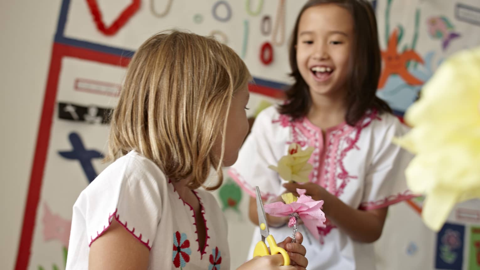 Young girls smile, hold tissue paper flower chain, craft scissors 