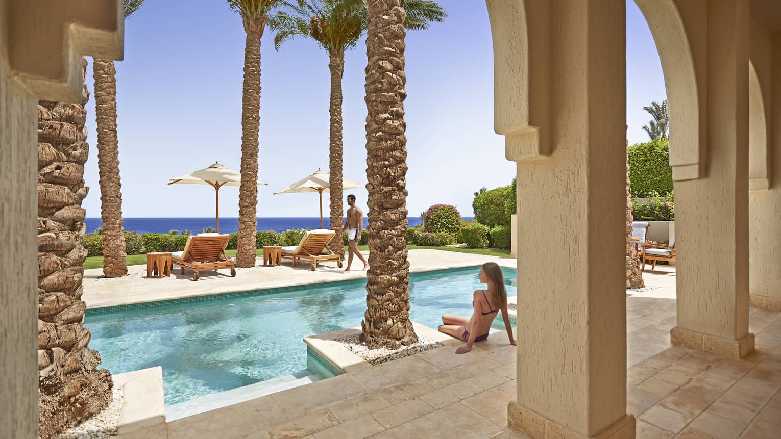Woman sitting at edge of pool, looking out to sea