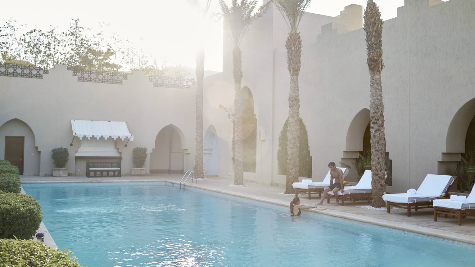 Couple relaxes poolside, row of lounge chairs and palm trees