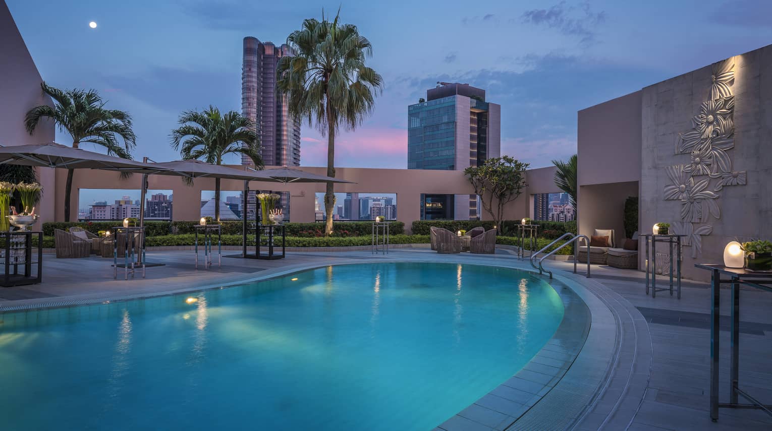 Sparkling rooftop pool at dusk, Singapore skyscrapers and palm trees in distance