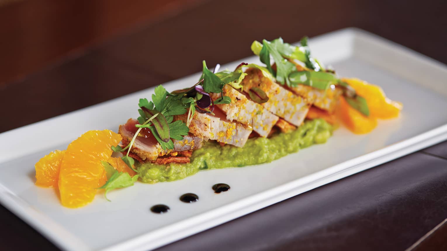 Sliced meat with green puree, spring lettuce, orange slices
