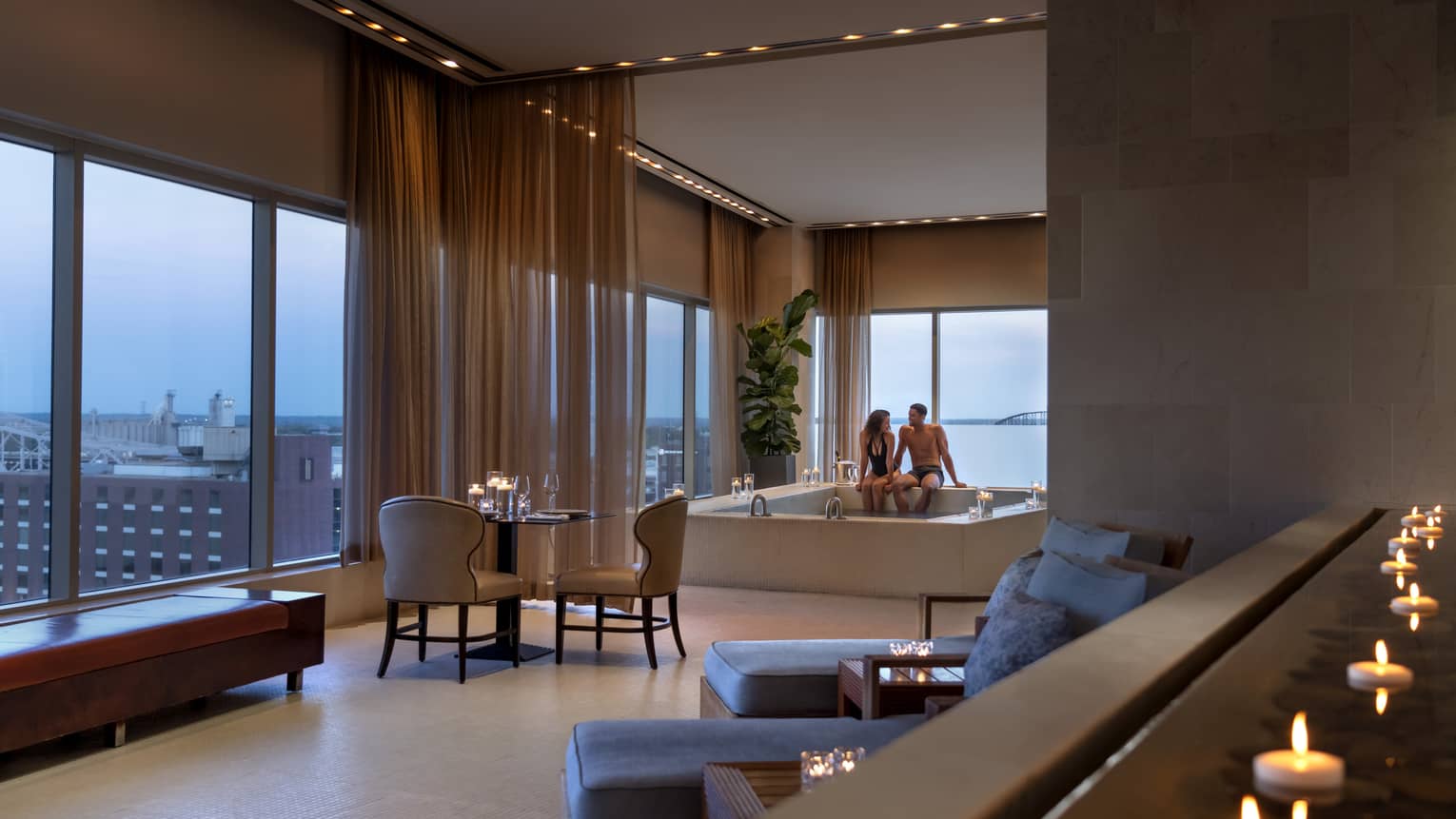A couple enjoying a candlelit hot tub in a luxury hotel spa, with elegant seating, soft lighting and large windows offering a view of a distant bridge