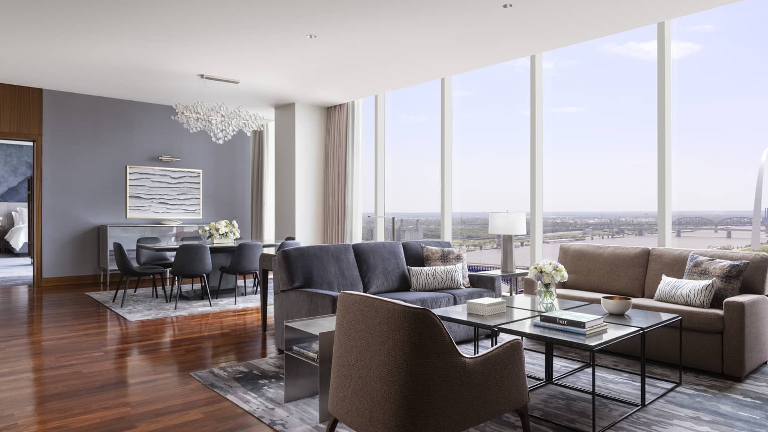 Suite living and dining area with two sofas, armchair, coffee table, dining table with chairs and large windows offering a view of the Gateway Arch and river