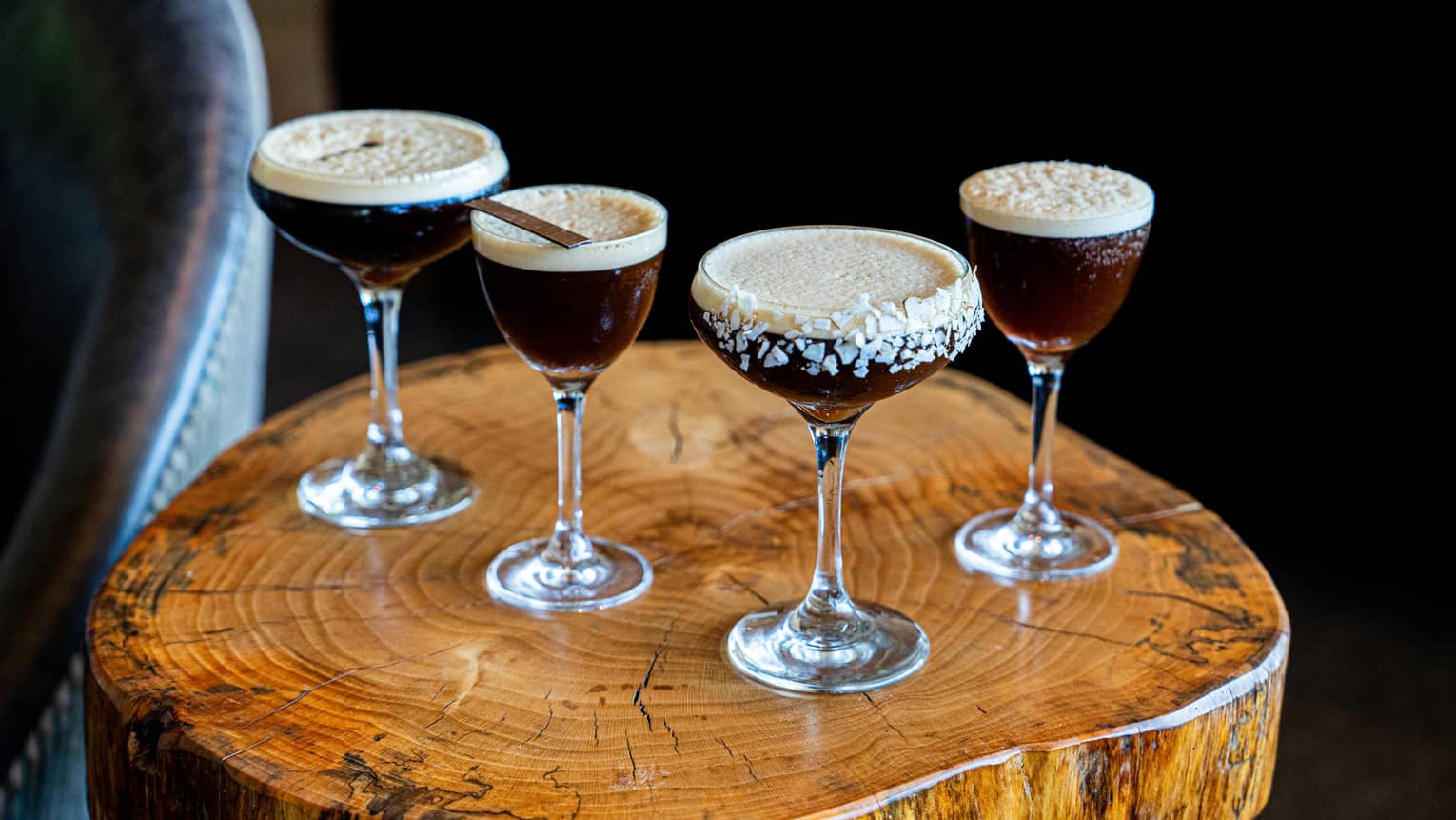 Four espresso martinis on a small wood table.