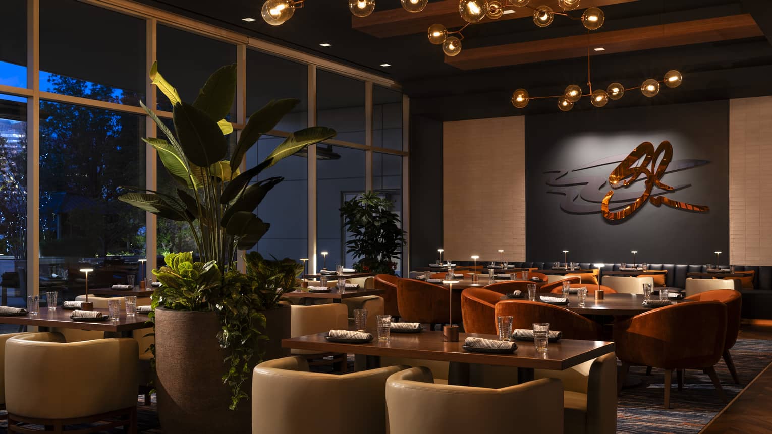 Elegant restaurant in a luxury hotel, featuring modern décor, warm lighting, plush seating and large windows with plants adding to the ambiance