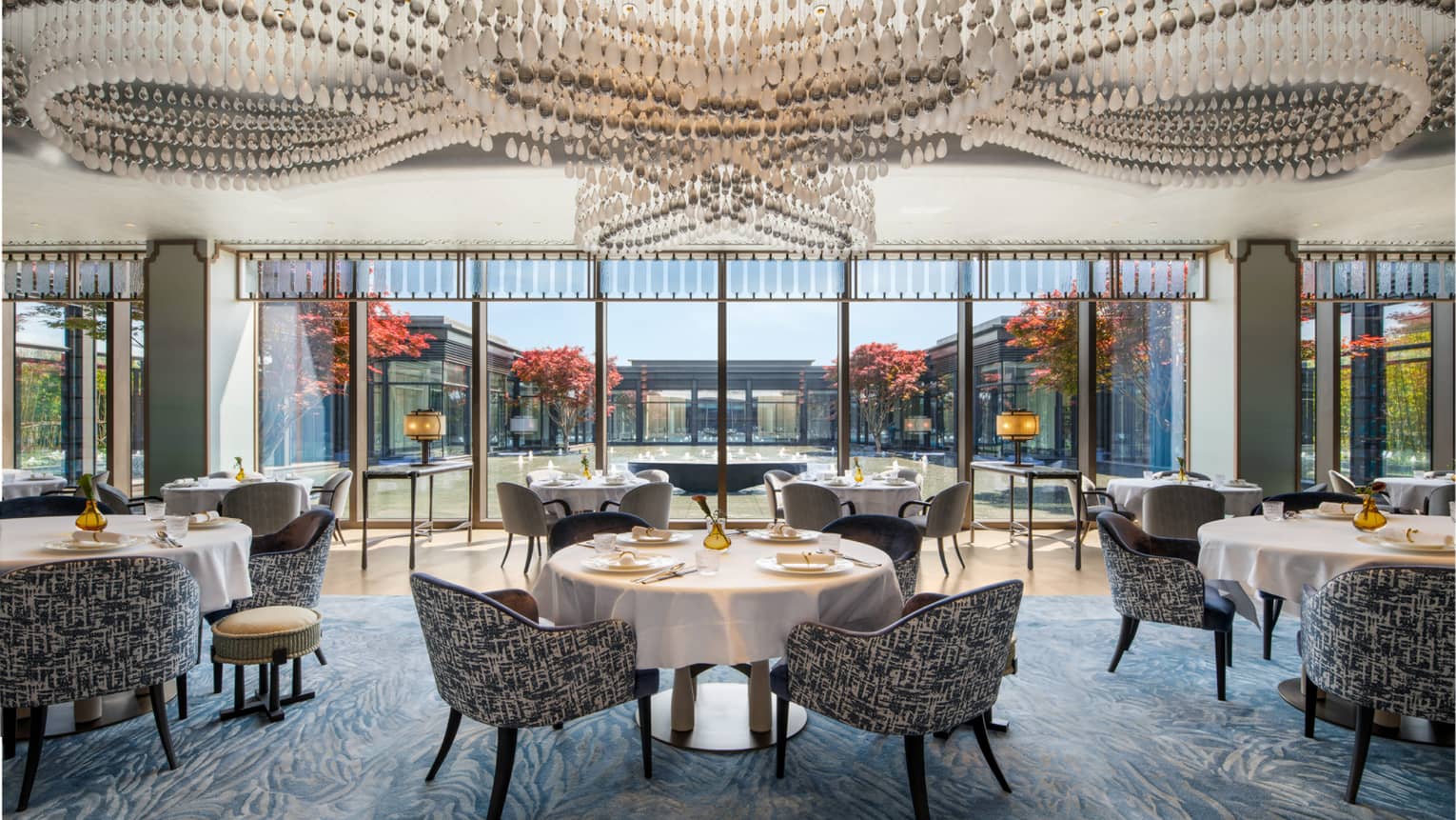 Jin Jing Ge restaurant at Four Seasons Hotel Suzhou. Dining tables with white tableclothes sit beneath a ceiling of modern chandeliers.