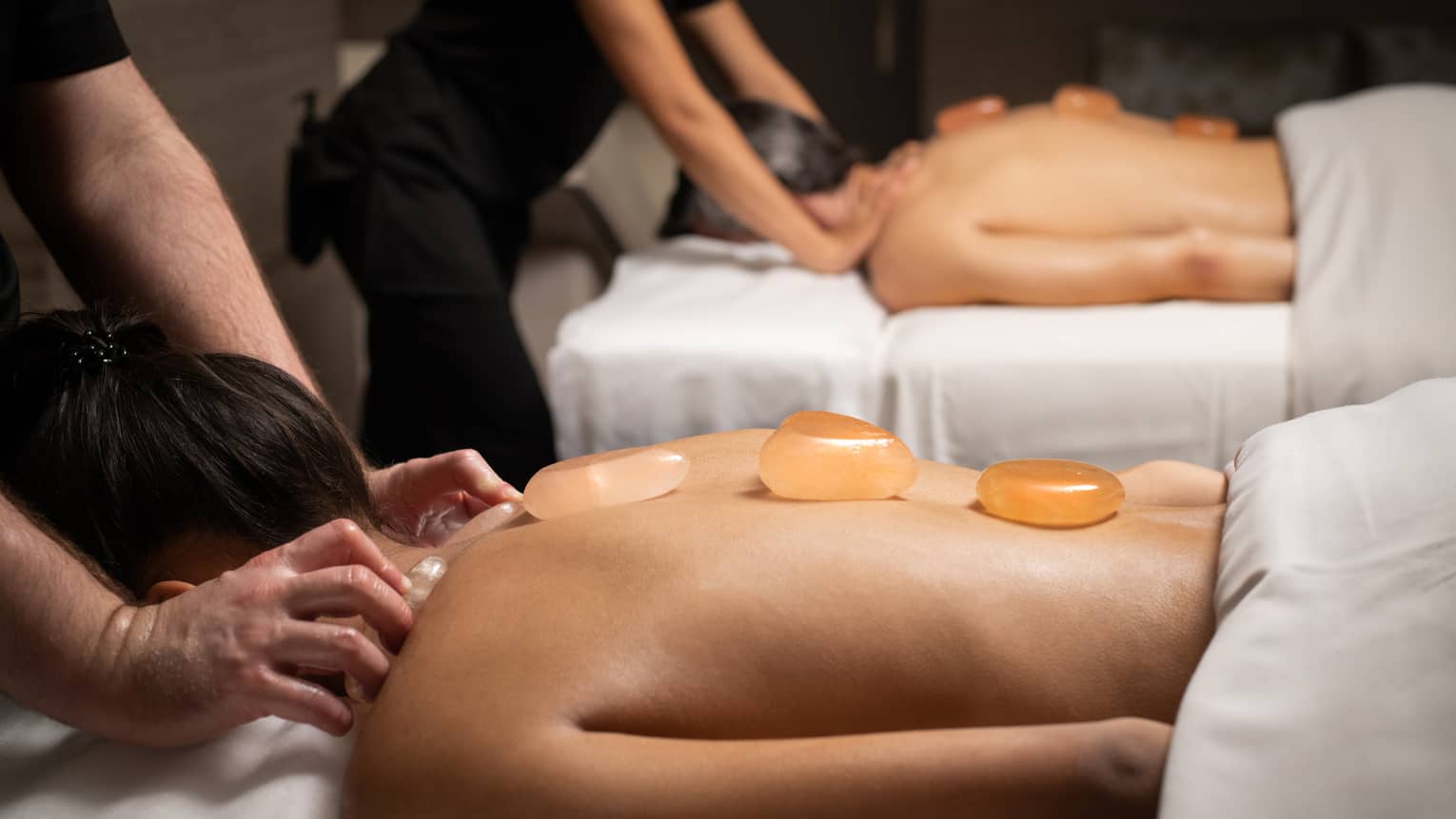 Two people getting a massage with small stones on their backs.