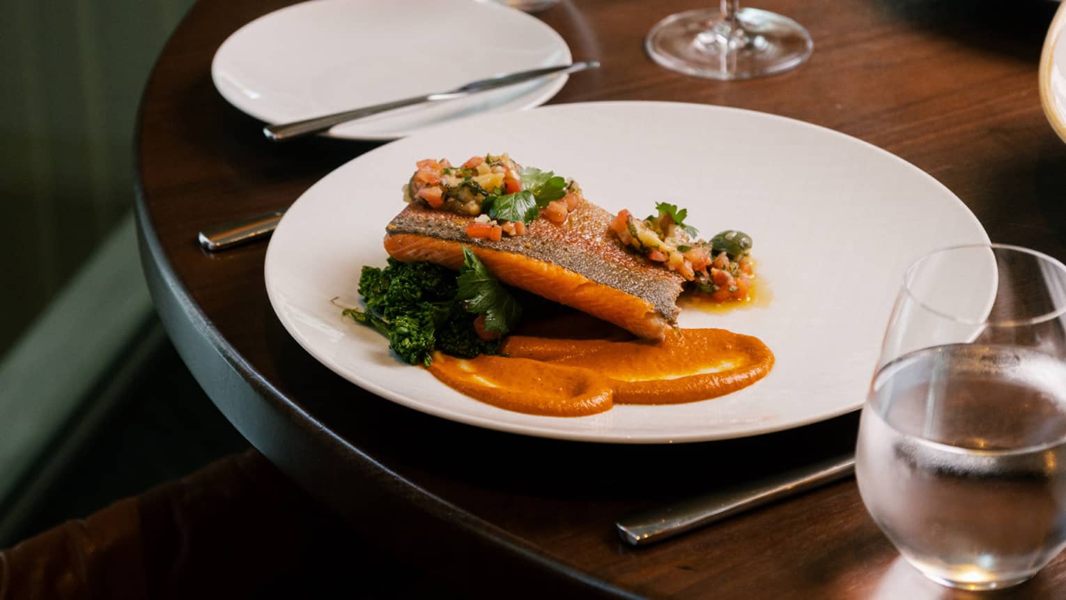 Cooked fish on an orange coloured sauce on a white plate.