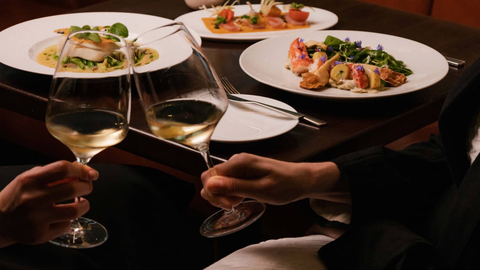 Two people clink glasses of white wine at restaurant table