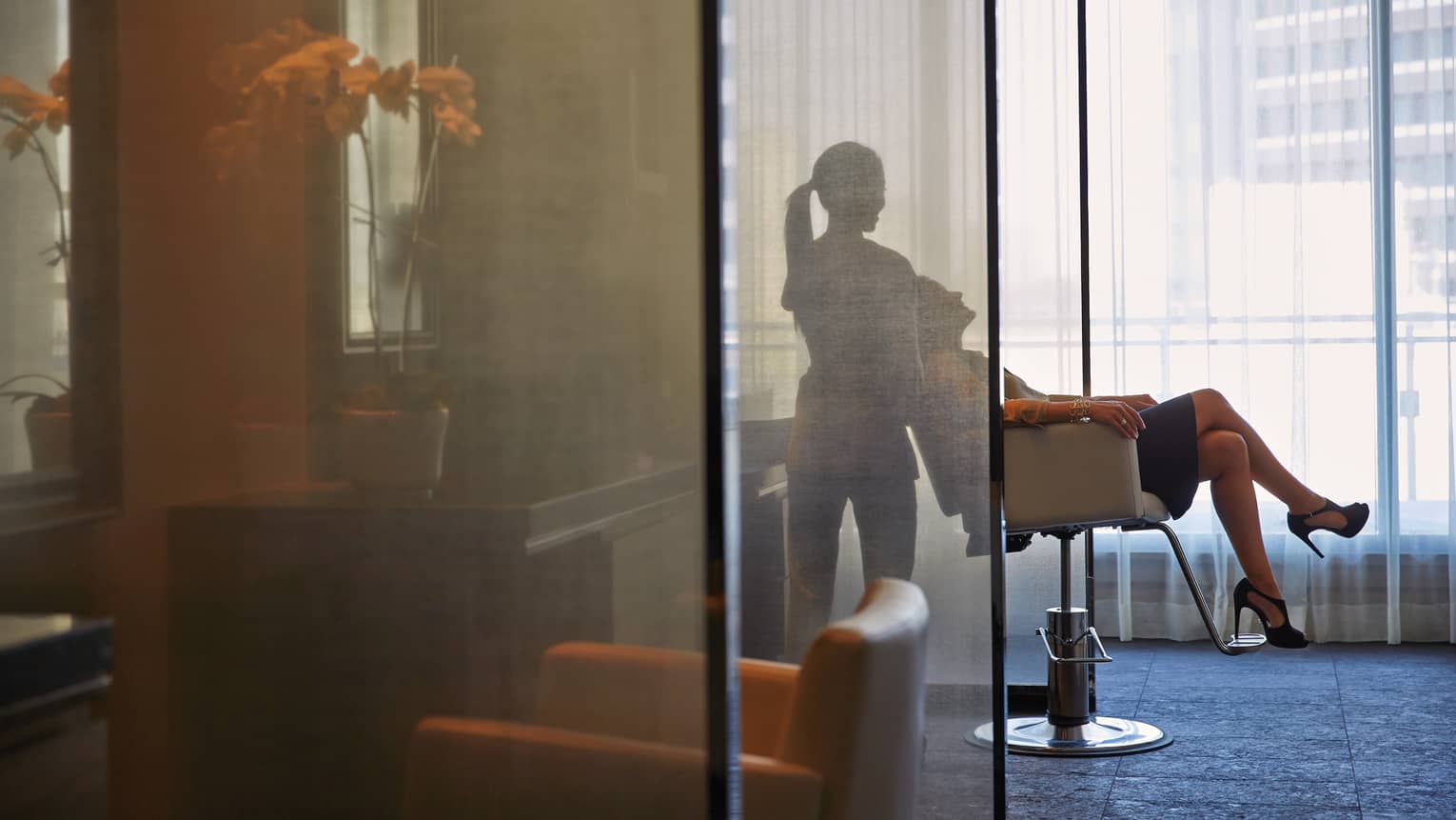 Silhouette of spa staff tilting woman back in salon chair behind sheer screen