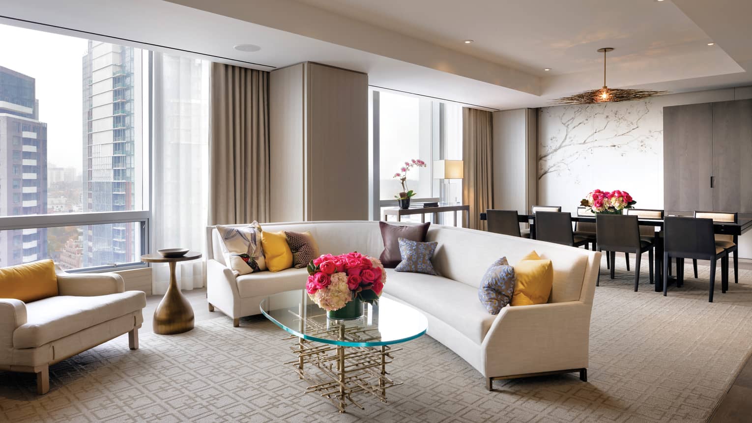 Bellair Suite curved L-shaped sofa, colourful pillows, chair under tall sunny windows, by long dining table