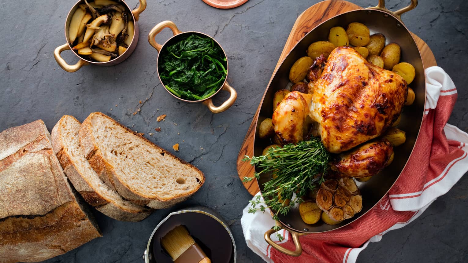 Aerial view of rotisserie whole chicken in roasting pan with herbs, fresh bread