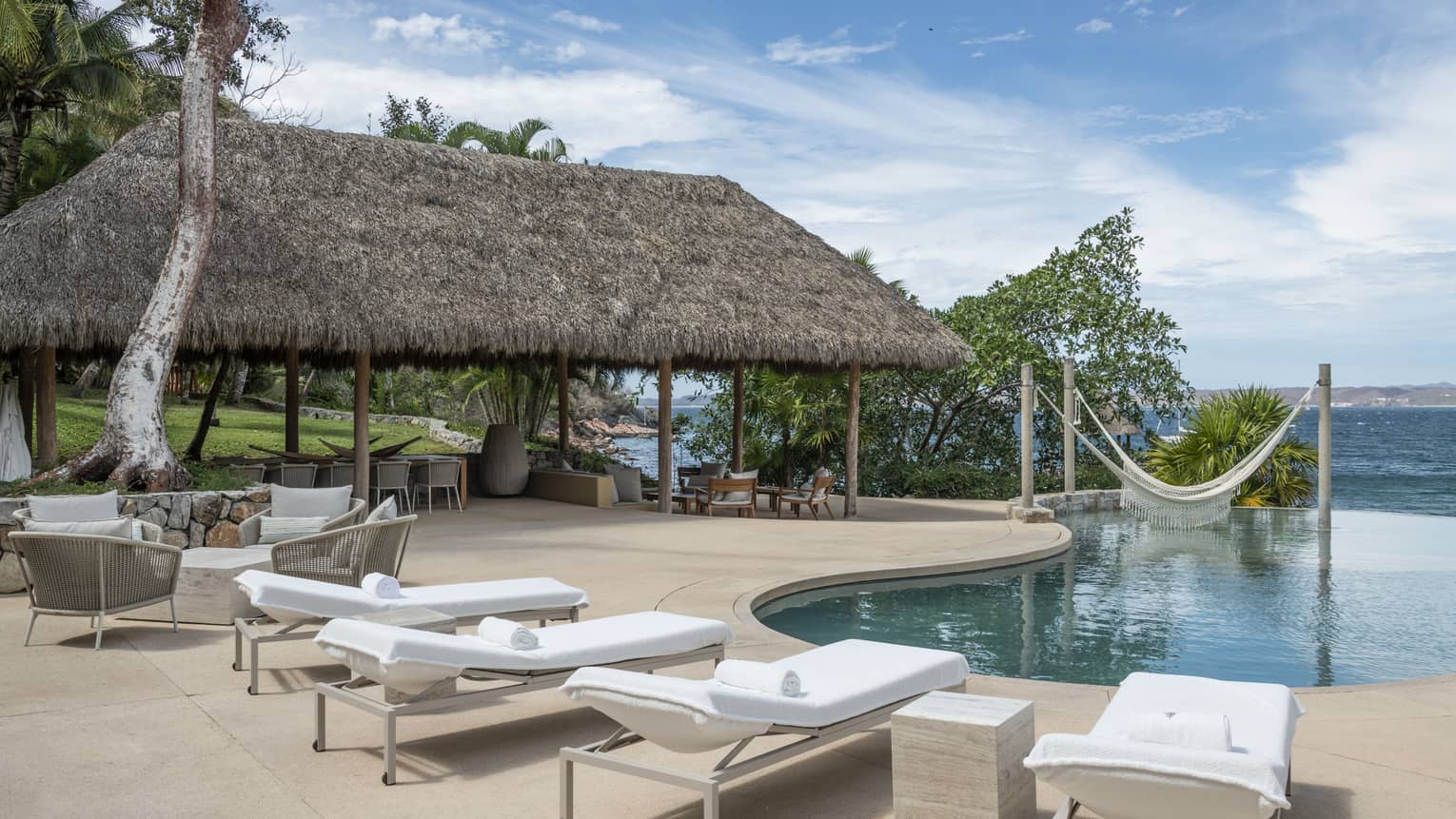 Private residence's pool terrace with four lounge chairs, dining area under a thatched-roof pavilion, and ocean views, at Four Seasons Resort Tamarindo