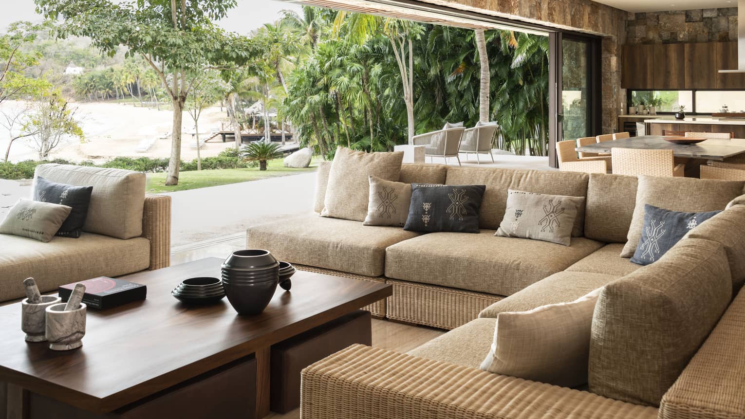 Large living room with rattan sectional sofa and coffee table. A massive wall completely opens to the outdoor terrace. Casa Vista at Four Seasons Resort Tamarindo.