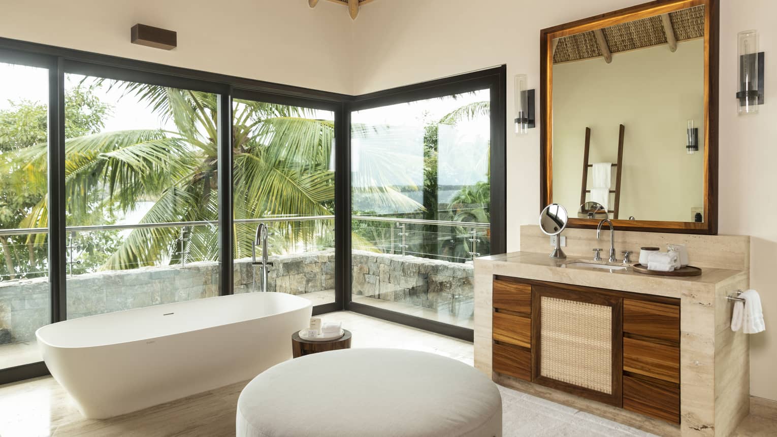 Large contemporary bathroom with ottoman bench, standalone tub, stone vanity and wrap-around windows looking out to tropical landscape at Four Seasons Resort Tamarindo