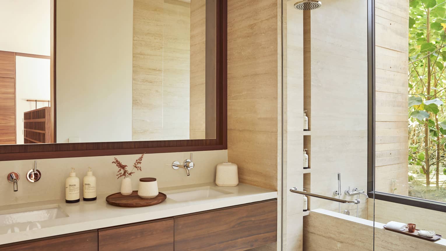 Elegant bathroom with a large mirror, double vanity and a walk-in shower beside a soaking tub. The space features neutral tones and opens to a view of greenery.
