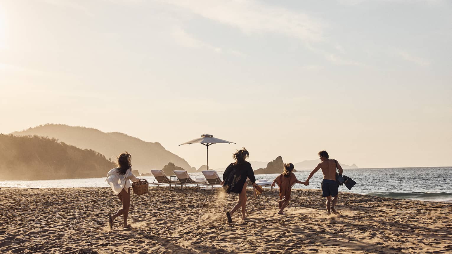 A group carrying various beach supplies runs across the sand toward the water, empty lounge chairs prepared for them. 