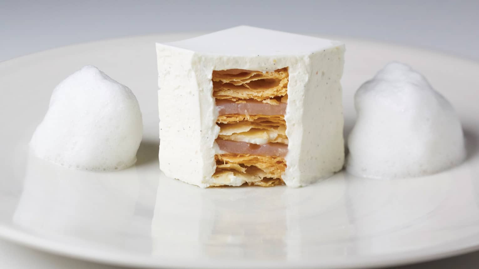 White foam flanks white millefeuille cut open in center, showing layers on white plate
