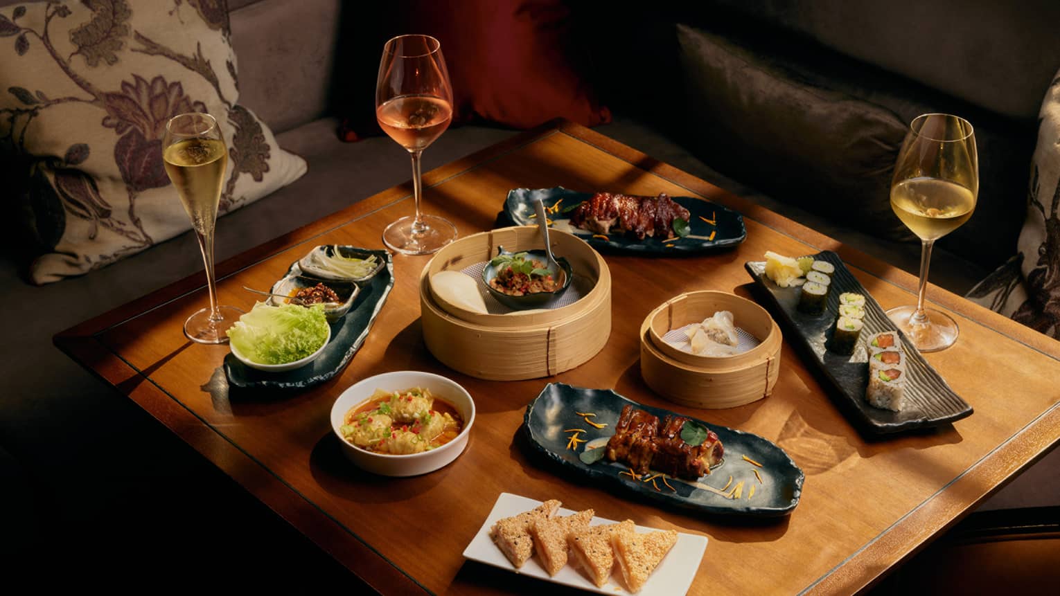 Assorted dim sum and glasses of wine on square wooden table