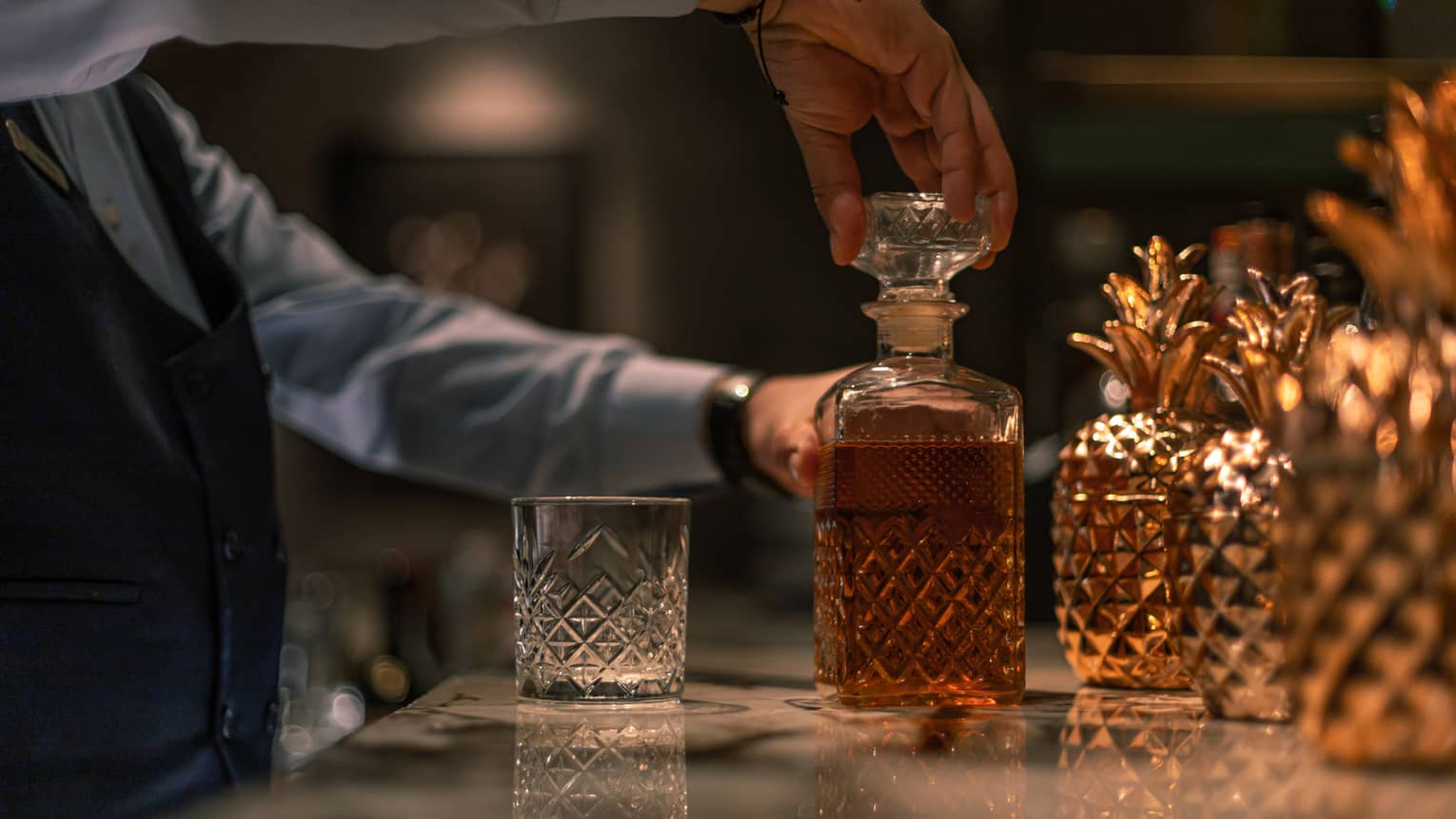 Bartender taking off bottle stopper from liquor-filled crystal decanter