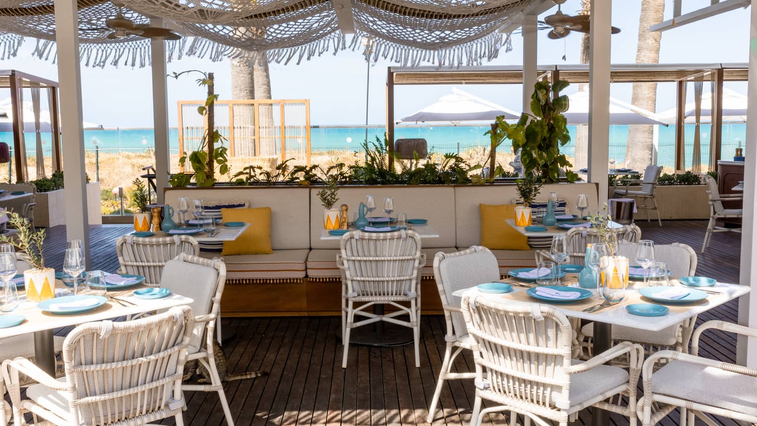 Restaurant terrace with white dining seating and banquettes with sea view in backdrop