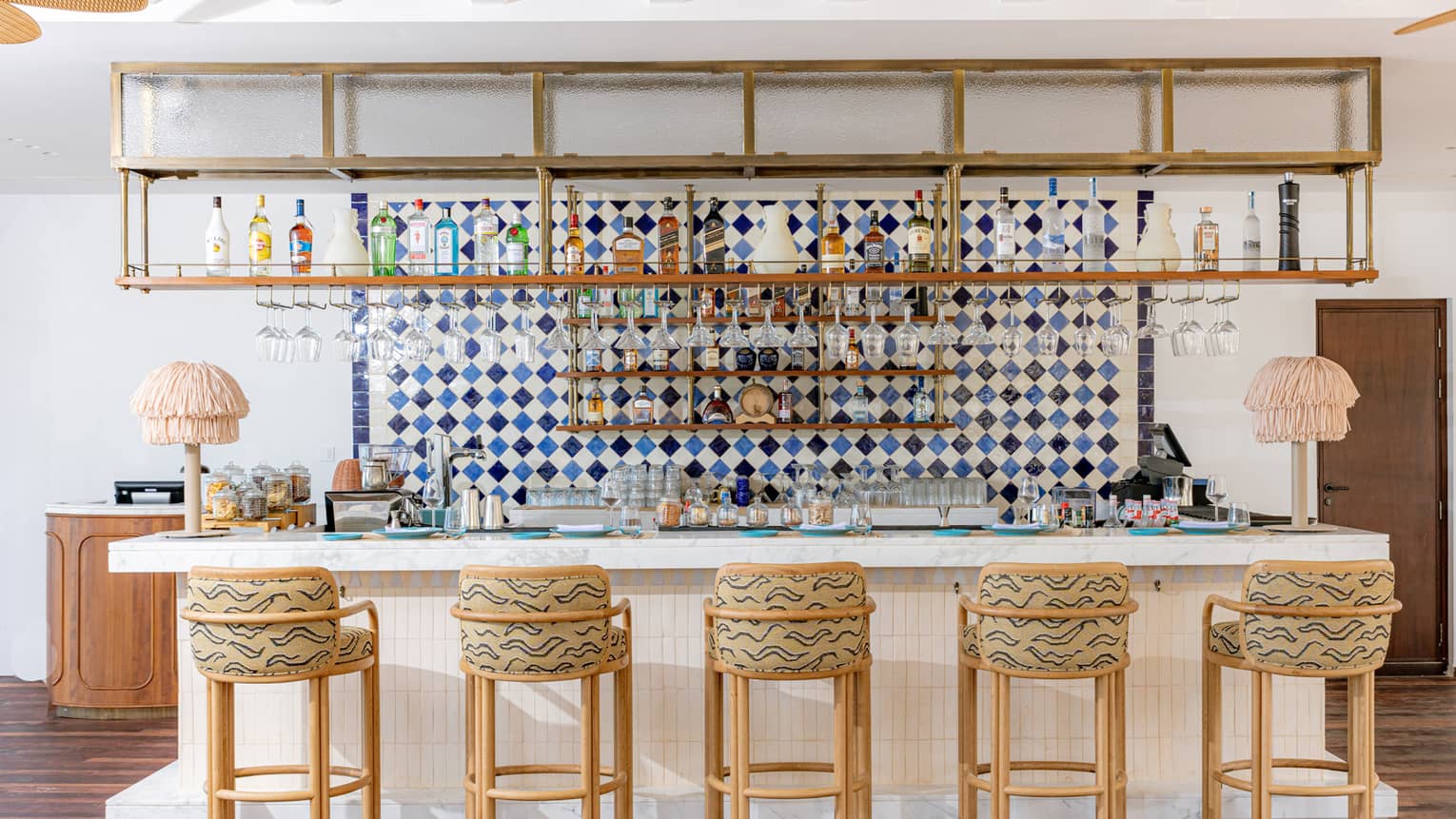 Restaurant bar lined with five bar stools underneath open shelving lined with liquor bottles