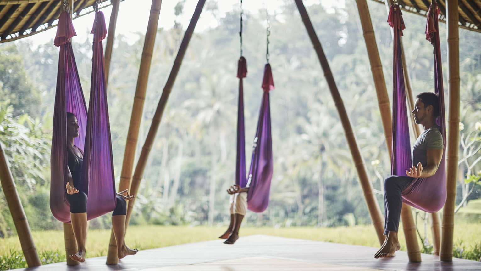 Guests sit in meditative poses within hanging silk hammocks suspended within an open-air bamboo pavilion.