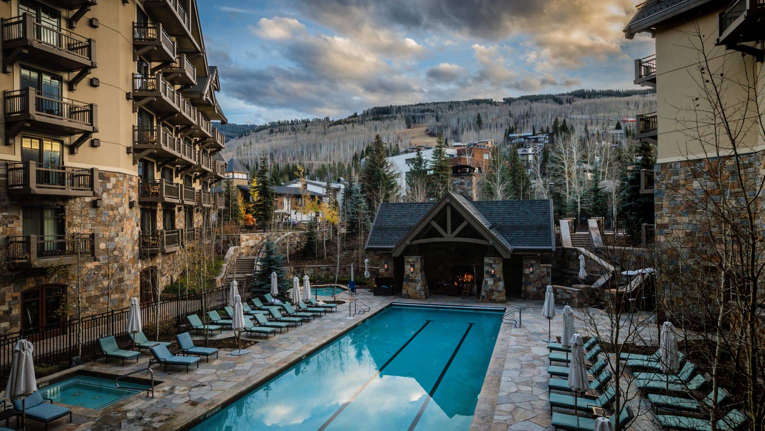 Blue lounge chairs face rectangle heated pool, surrounded by hotel building and mountain views