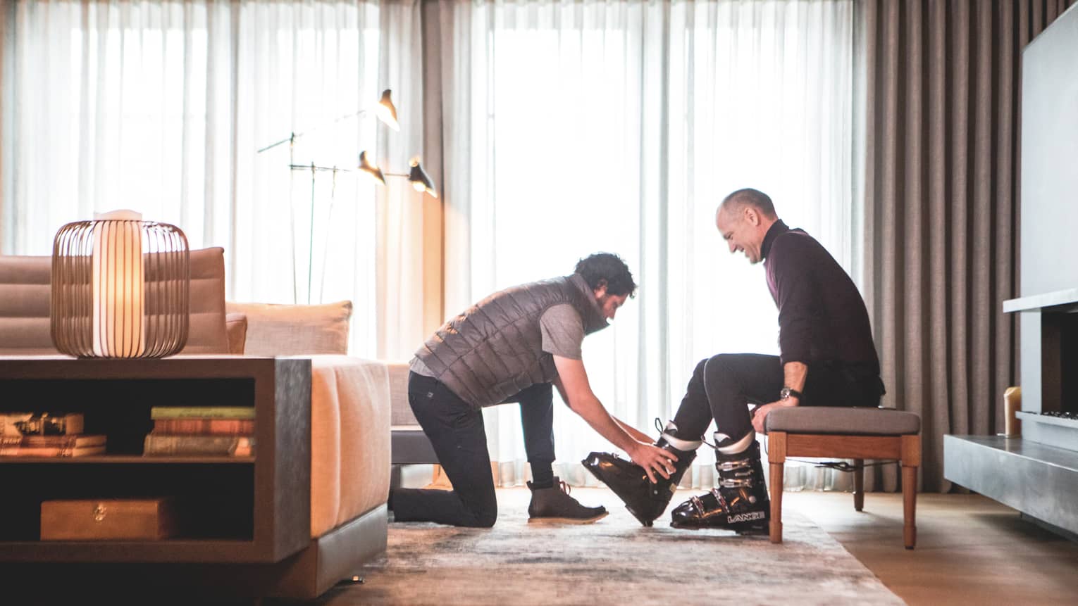 One man helping another to put on ski shoes.