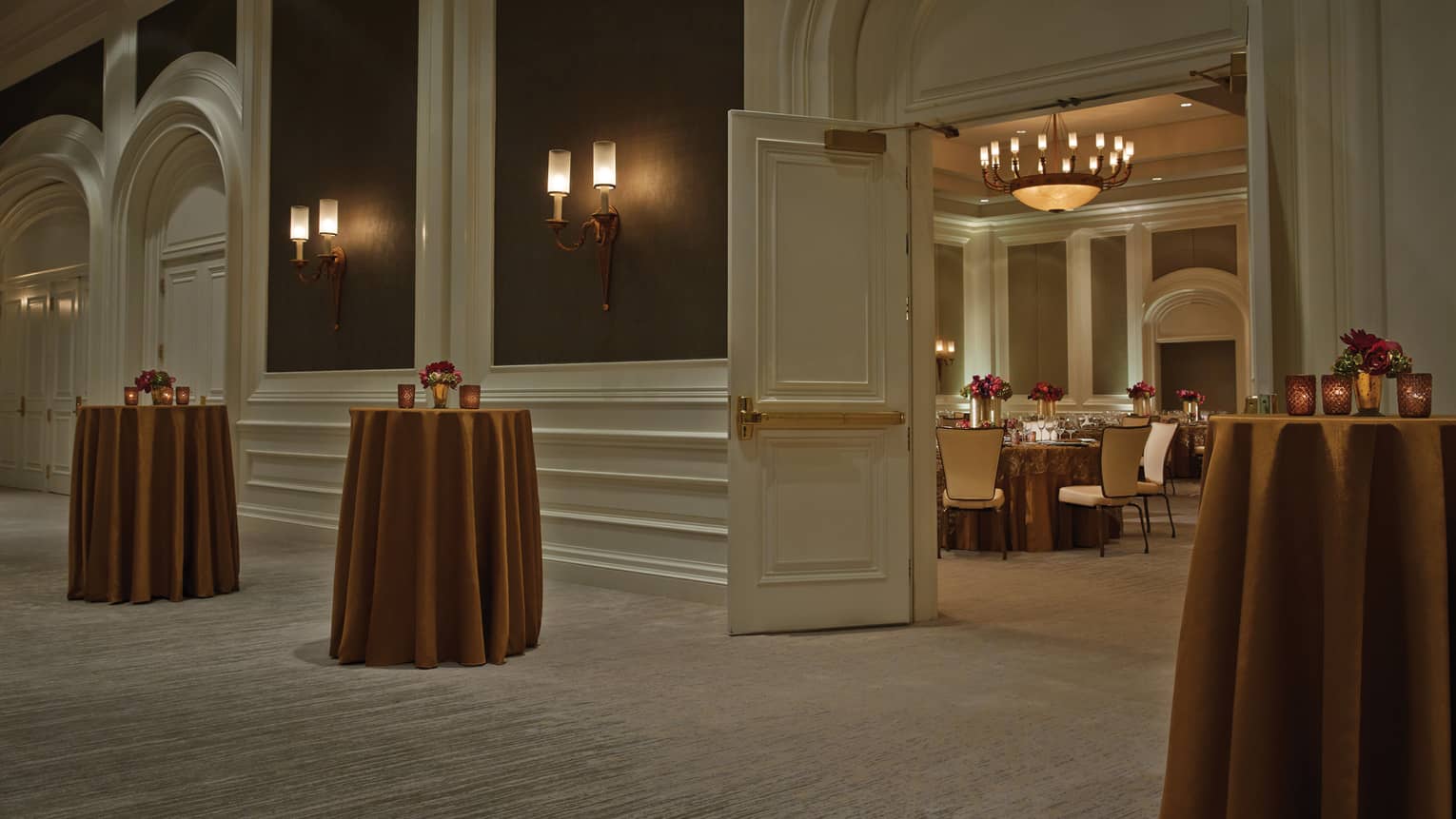 Small cocktail tables with brass-coloured linens by open doors to Acacia Ballroom