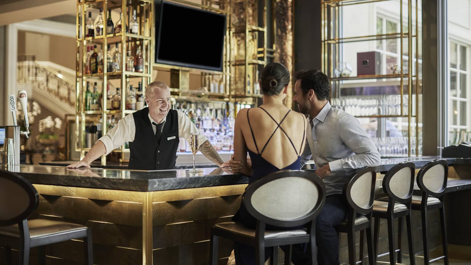 Smiling bartender greets couple sitting on stools at bar